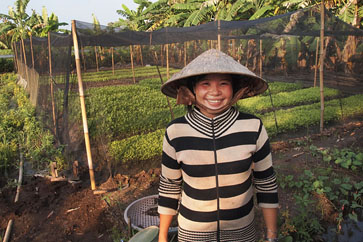 A loan recipient in front of her environmentally friendly net greenhouse.