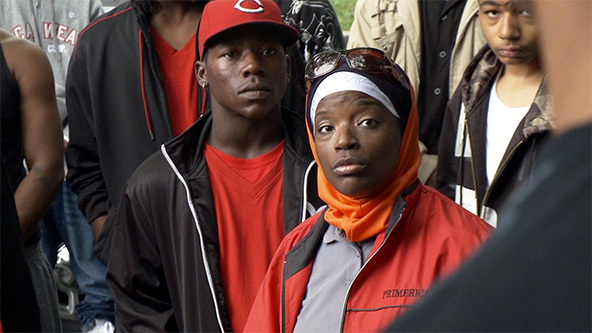 Black woman in red jacket standing with Black man in red shirt, black jacket