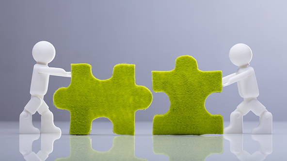 Two figures pushing puzzle pieces together to represent a merger.