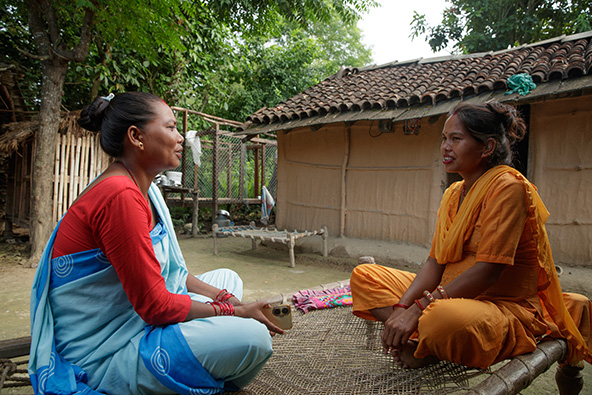 two women wearing saris, seated, talking with each other