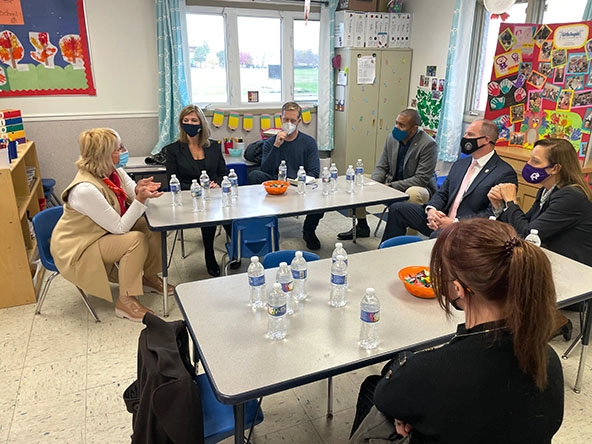Women and men sitting at preschool tables in a classroom.