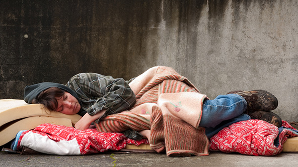 Homeless woman sleeping with blankets and a foam mattress on the street