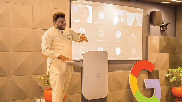 Man stands at podium next to screen and Google logo