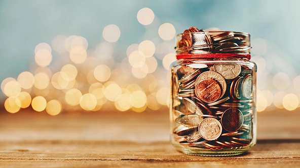 Donation money jar filled with coins in front of holiday lights 