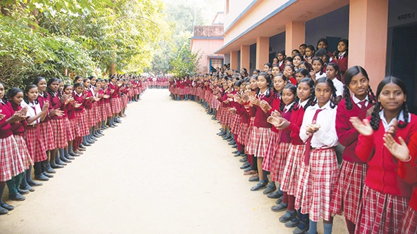 Rows of girls in school uniforms stand outside a school building