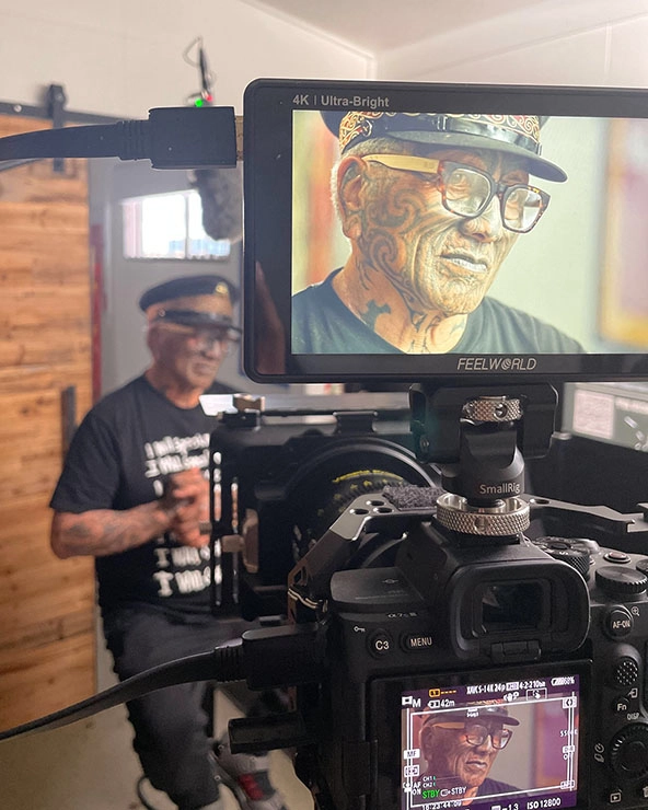 Indigenous man wearing a hat standing in front of a video camera.