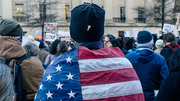 person with american flag wrapped around shoulders in front of government building