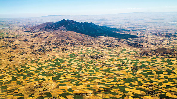 An aerial view of hills and rural farmland dotted with green and golden-colored patches of land