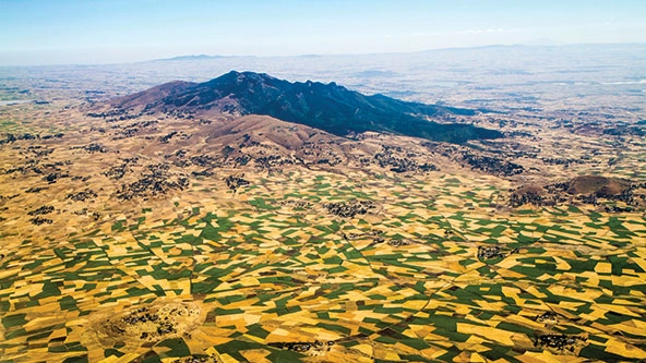 An aerial view of hills and rural farmland dotted with green and golden-colored patches of land