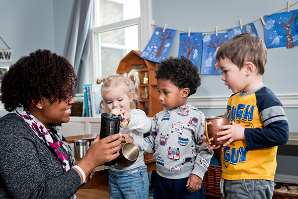 Woman in a classroom with young children holding cups