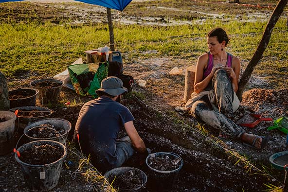 two archaeologists sitting at a dig site under a tent