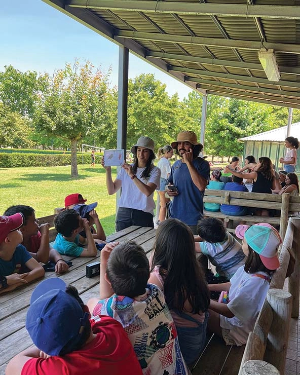 Young children sitting at a picnic table listen to adults teach about biodiversity; referenced in article