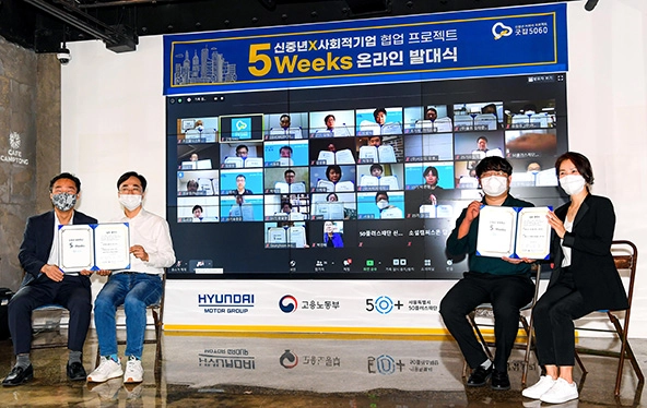 Four people sitting in front of a large screen with faces of people on computer screens. The words 