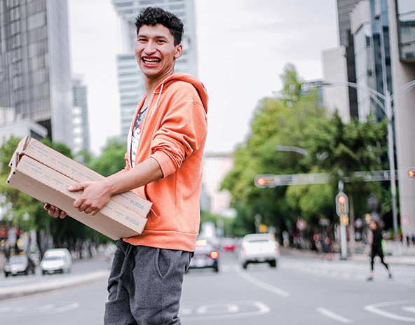 Youth walking across street carrying pizza boxes.