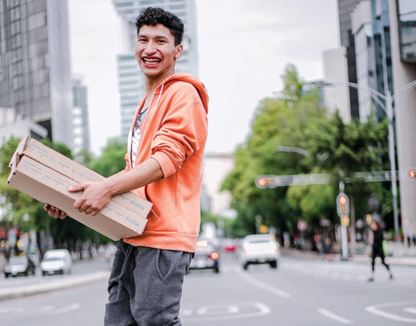 Youth walking across street carrying pizza boxes.