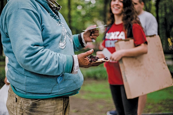 Homeless person stands with slick of pizza in their hands.