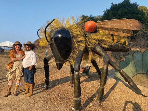 Two people standing next to a sculpture of a bee.