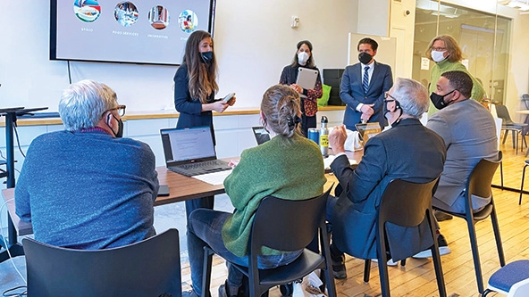 Four people standing and making a presentation to four people seated at a table.