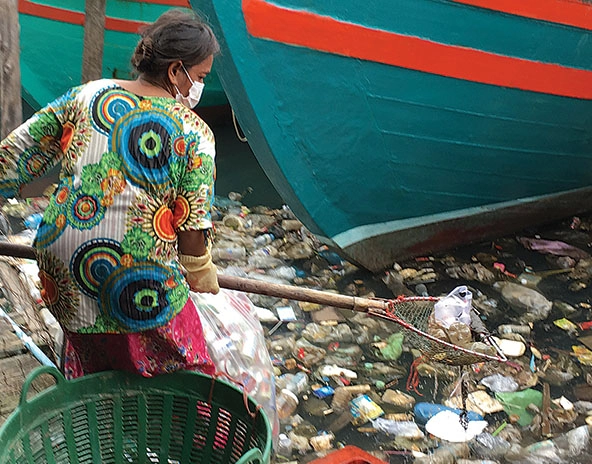 Woman using a net to pick plastic out of water.