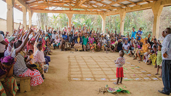 People sitting in a pavilion raising hands to take a vote