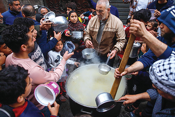 Palestinian man serving soup from a large pot surrounded by people