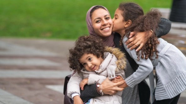 Muslim mother hugging her daughters in a park.

